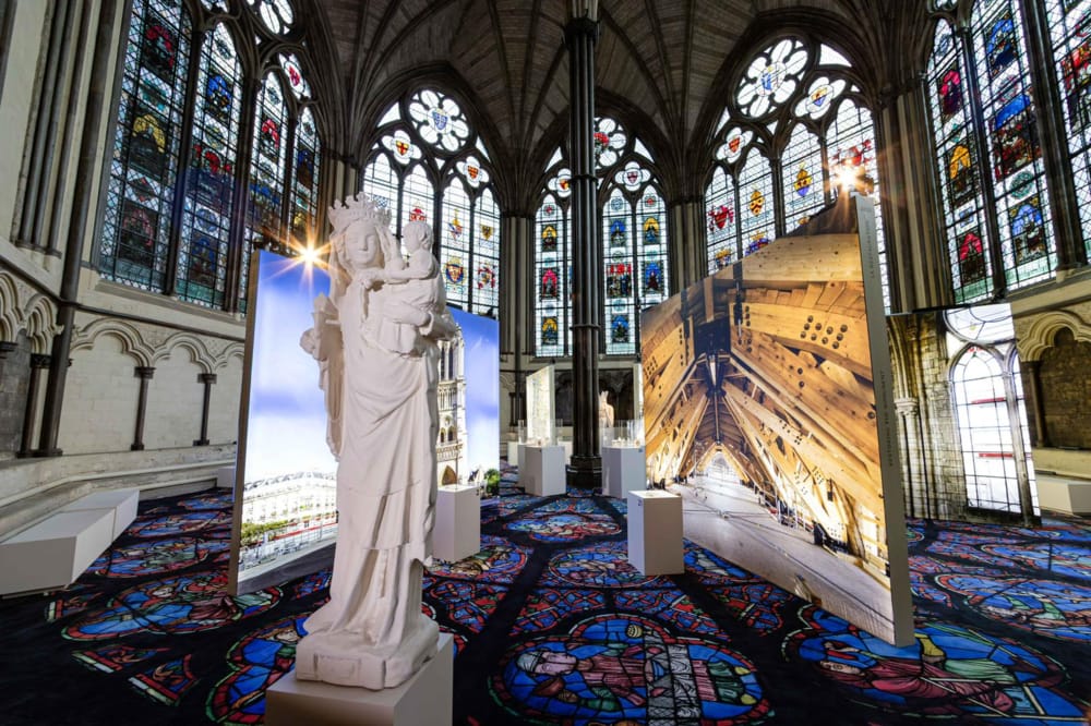 Larger photos of Notre Dame and a religious statue are displayed inside a London church with stained glass windows.