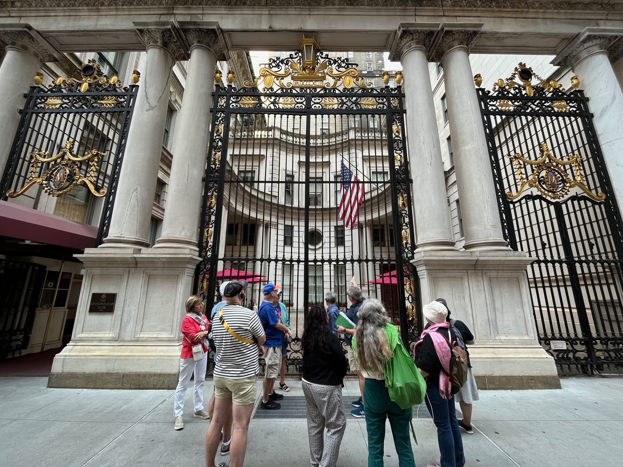 A group of tour goers stand outside a black and gilded gate on 5th Ave