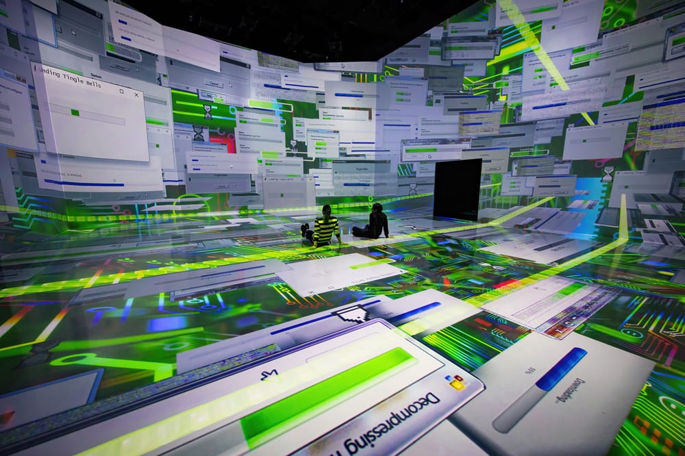 A person stands Two people stand in a room with walls covered in digital projections of computer windows