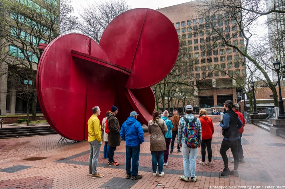 A tour group stands in front of a large red sculpture in Brooklyn