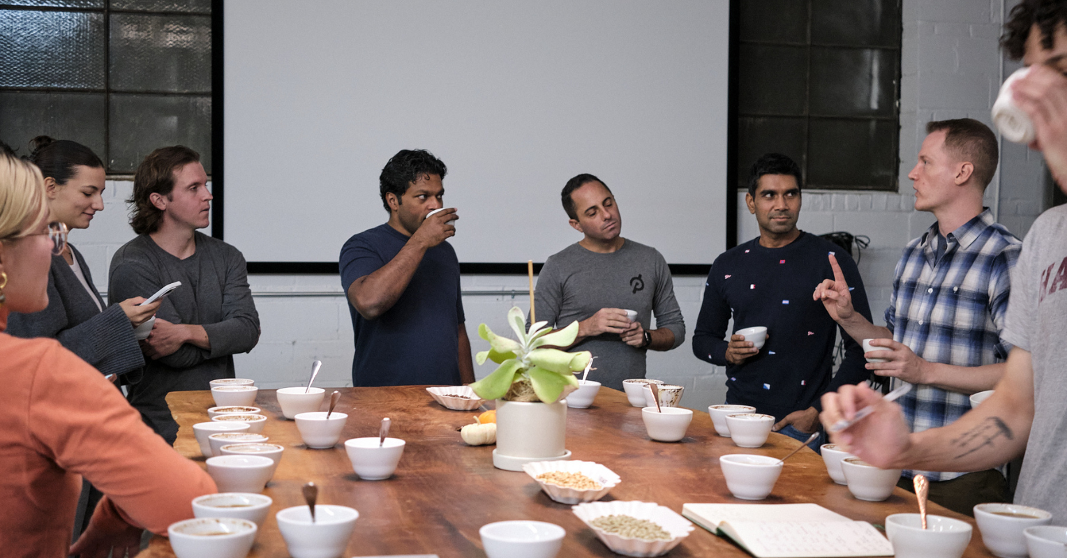 A group of people stand around a table covered in coffee cups at a coffee tasting event