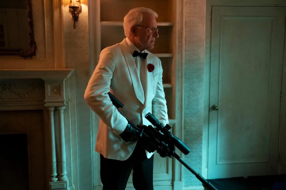 Steven Martin holds a sniper gun while wearing a white suit