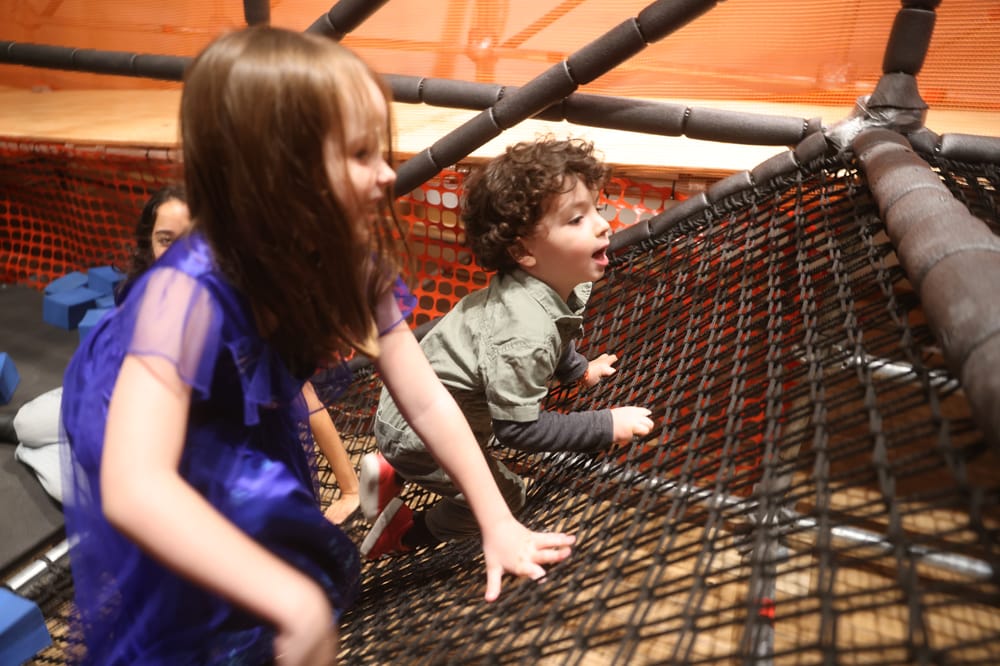 Small kids climb up a rope wall on a scaffolding playground