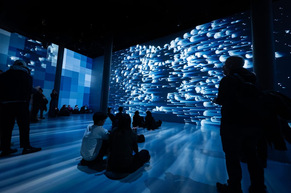 People sit on the floor and look at a projection of abstract blue streaks at ARTECHOUSE NYC