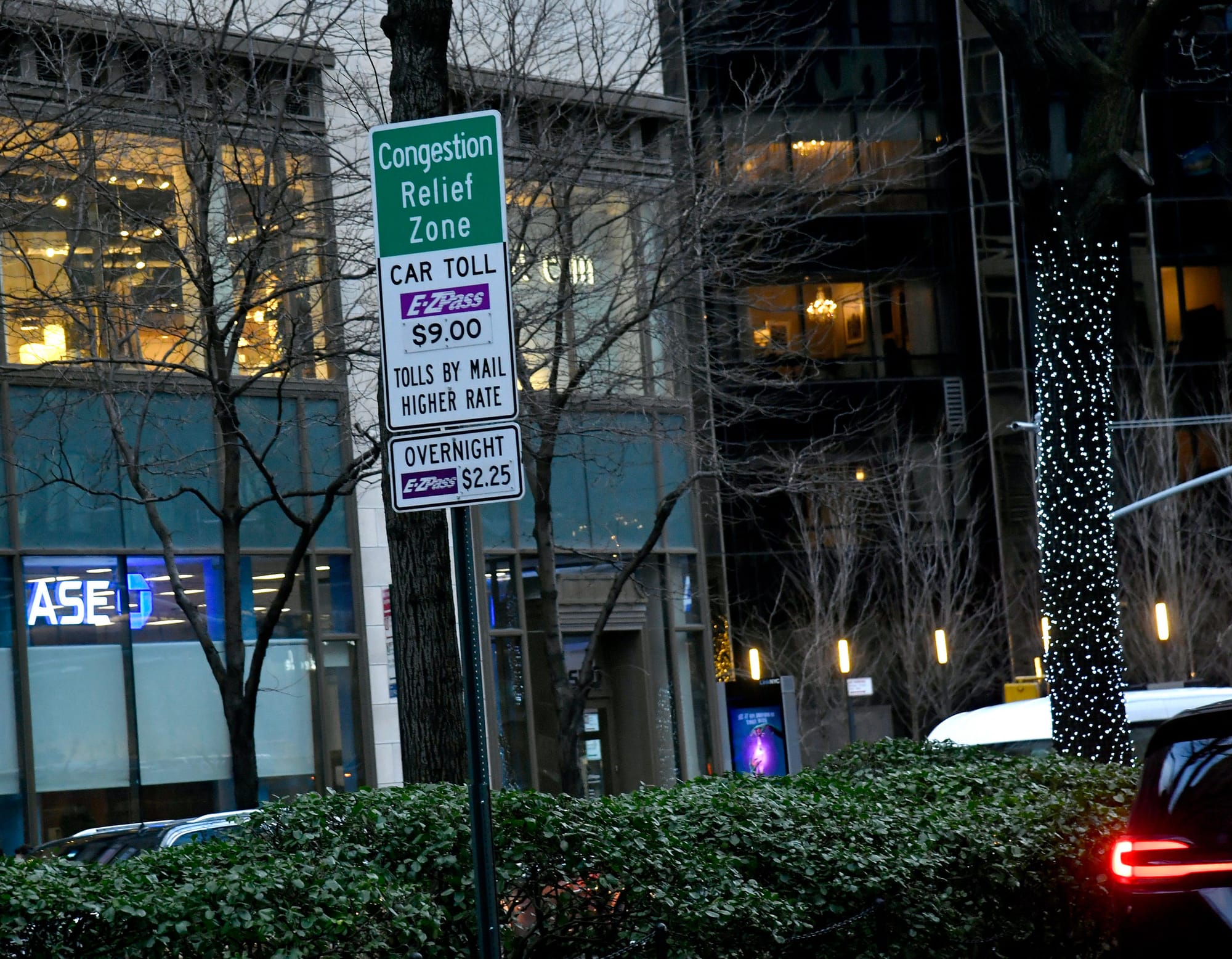 A street sign that reads "Congestion Relief Zone Car Toll E-Z Pass $9.00 Tolld by Mail Higher Rate Overnight E-Z Pass $2.25"