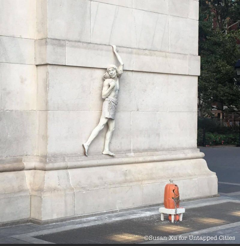 A man painted in white stands against the Washington Square Arch