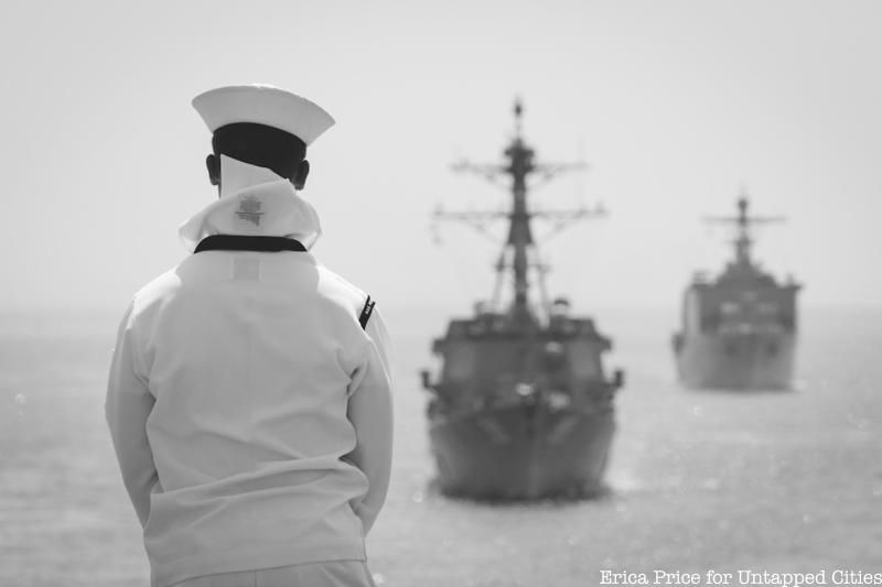 A Navy member stands facing two incoming ships