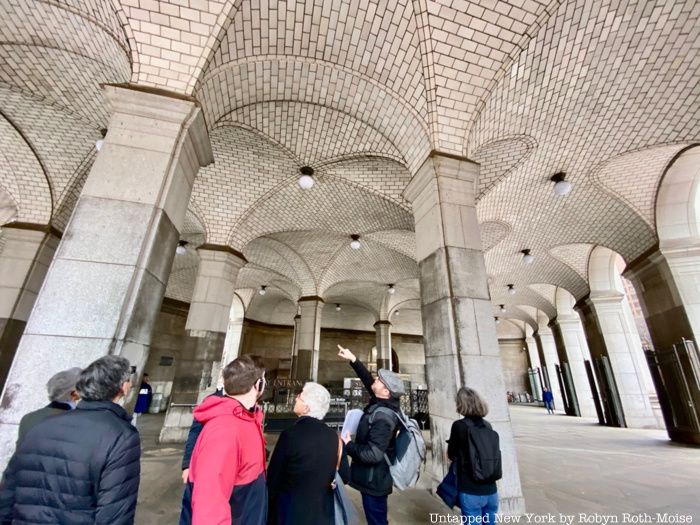 A group of tour guests look up at Guastavino tiles at the entrance to a subway station.