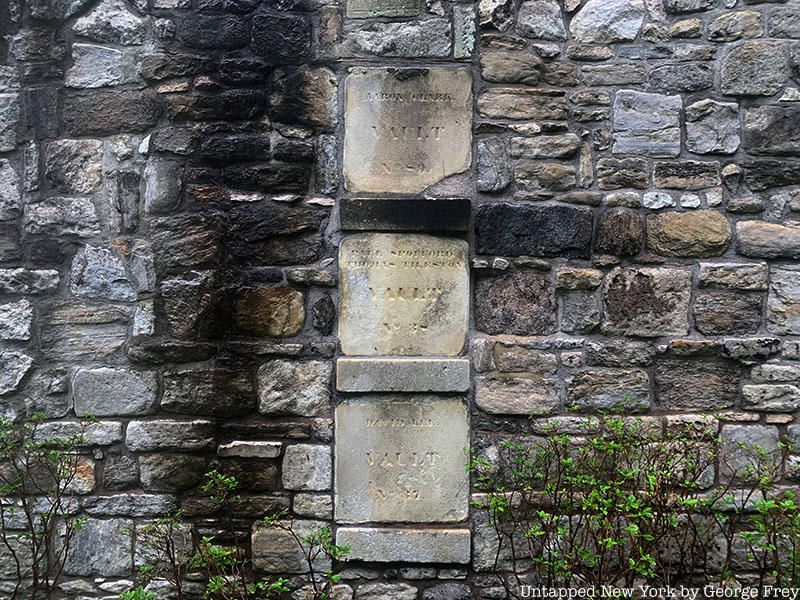 A stone wall at New York Marble Cemetery adorned with white marble plaques.