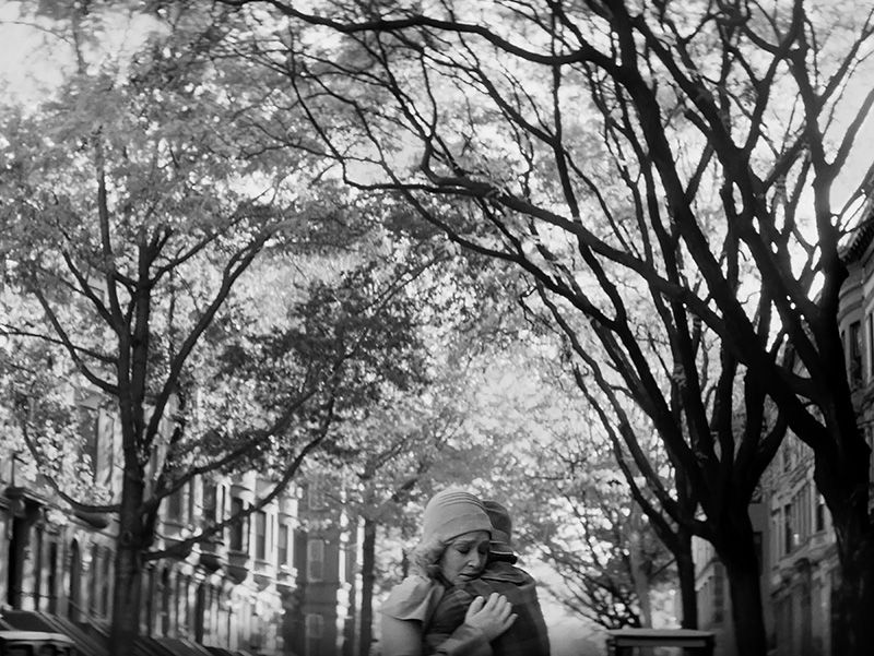 two women embracing on a tree-lined street