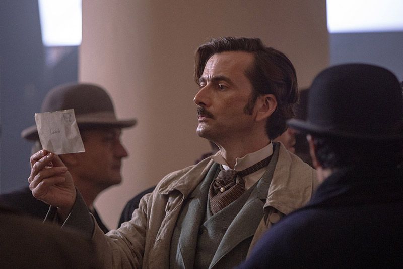 David Tenant as Phileas Fogg looking at postcard in train station