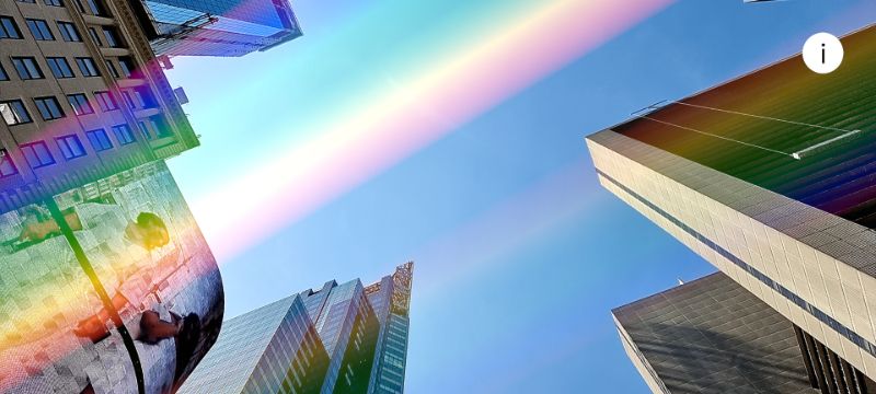 A rainbow made of light stretches across the daytime sky over Times Square. 