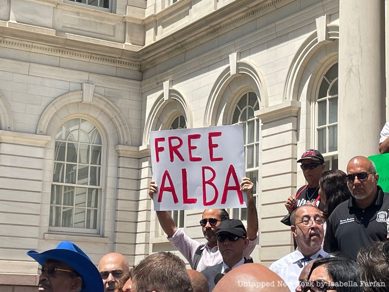 Man holding "Free Alba" sign during press conference on the steps of City Hall 