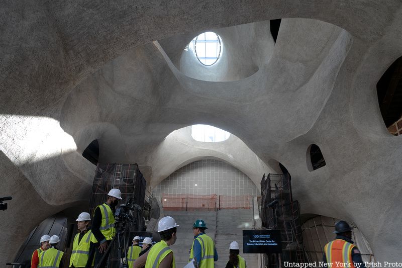 People in hardhats and yellow vets admire the construction of the Gilder Center atrium