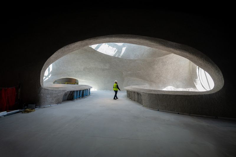 A construction worker is surrounded by shadows as he stands in the light of a skylight in the Gilder Center