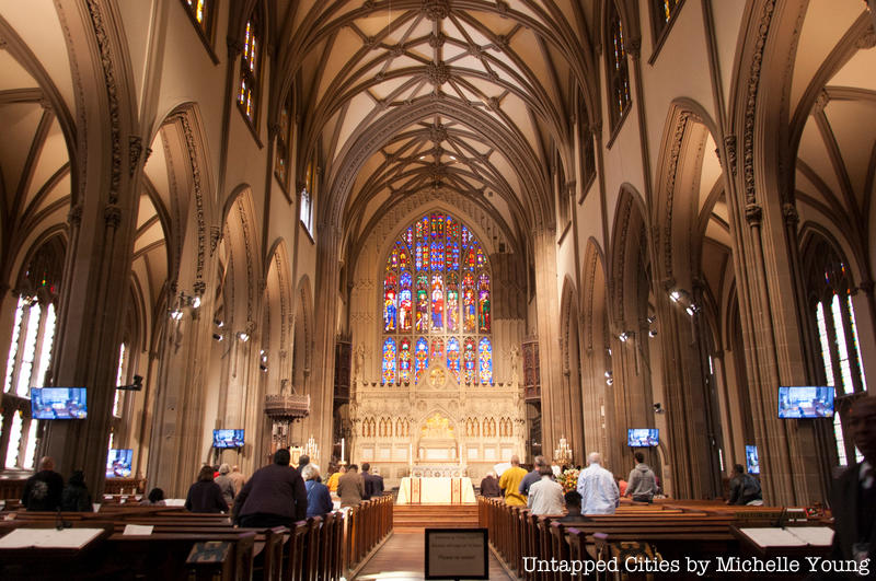 The nave of Trinity Church Wall Street featuring a colorful stained glass window and gothic arches.