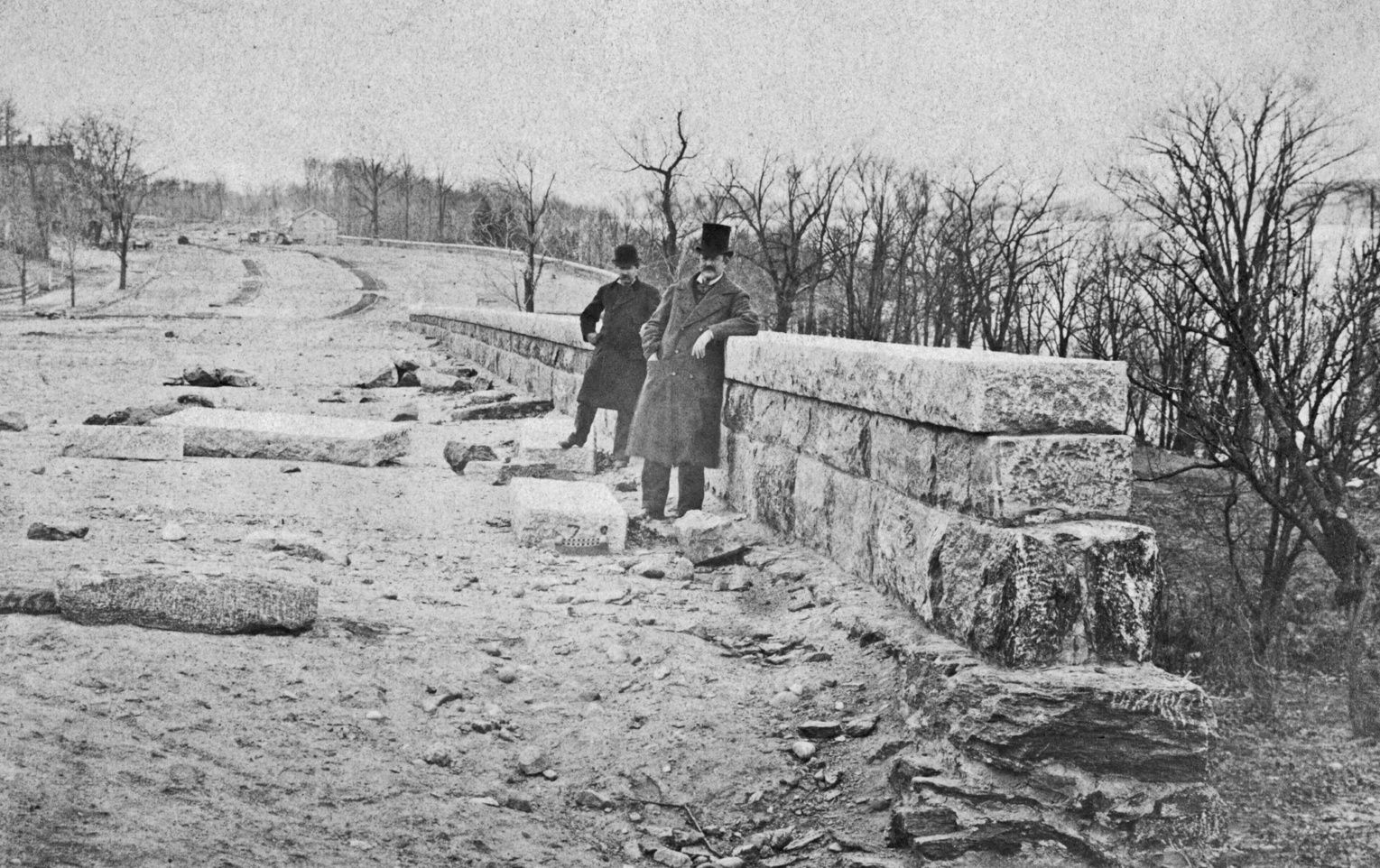 Two men stand at an unfinished stone wall in a black and white photo of Riverside Park