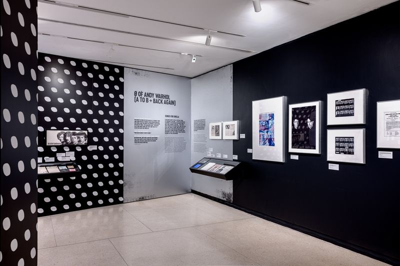 Black, grey and white polka dot walls covered in items related to The Velvet Underground and Andy Warhol at an NYPL exhibit