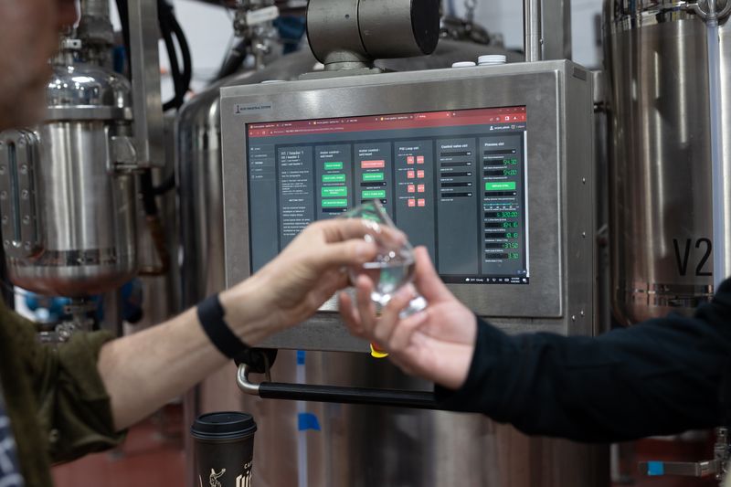 One hand passes an empty glass to another hand in front of a digital control panel