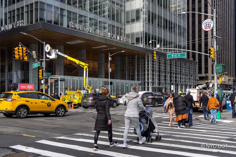 People crossing a NYC street below a country medallion on Sixth Avenue