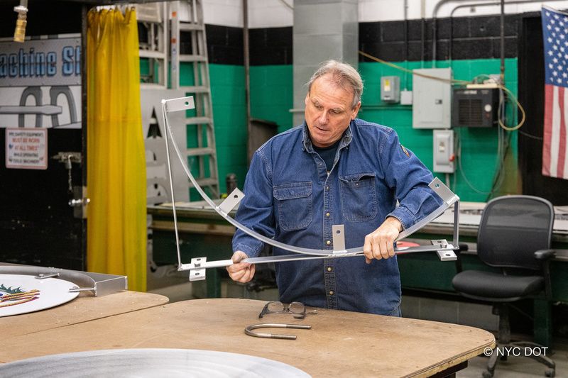 A worker inside the DOT Sign Shop fixes a metal bracket