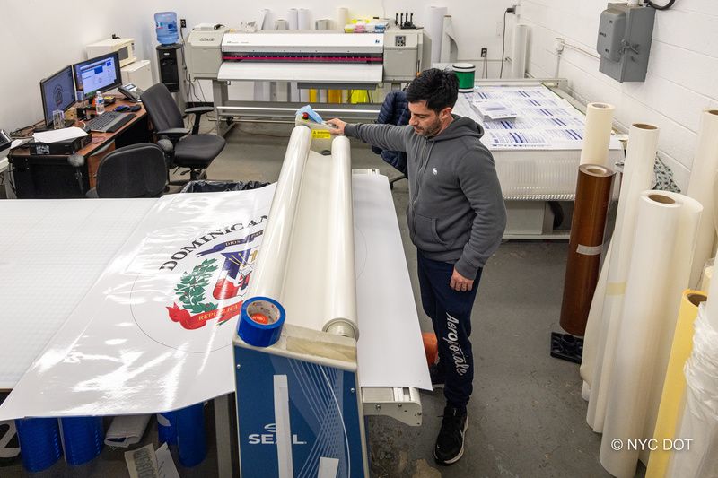 A worker at the DOT Sign Shop rolls out a sticker for an Avenue of the Americas medallion