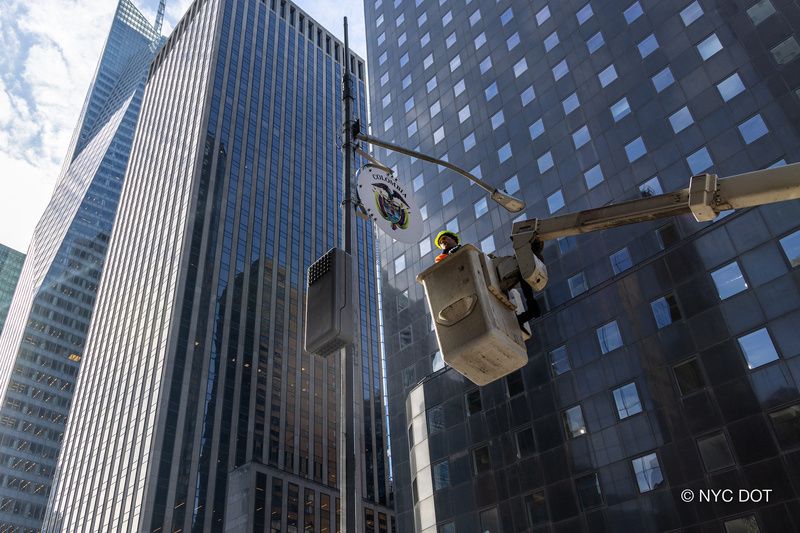 A worker in a cherry picker installs a sign on a lamppost