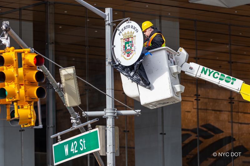 A worker in a cherry picker installs a sign on a lamppost