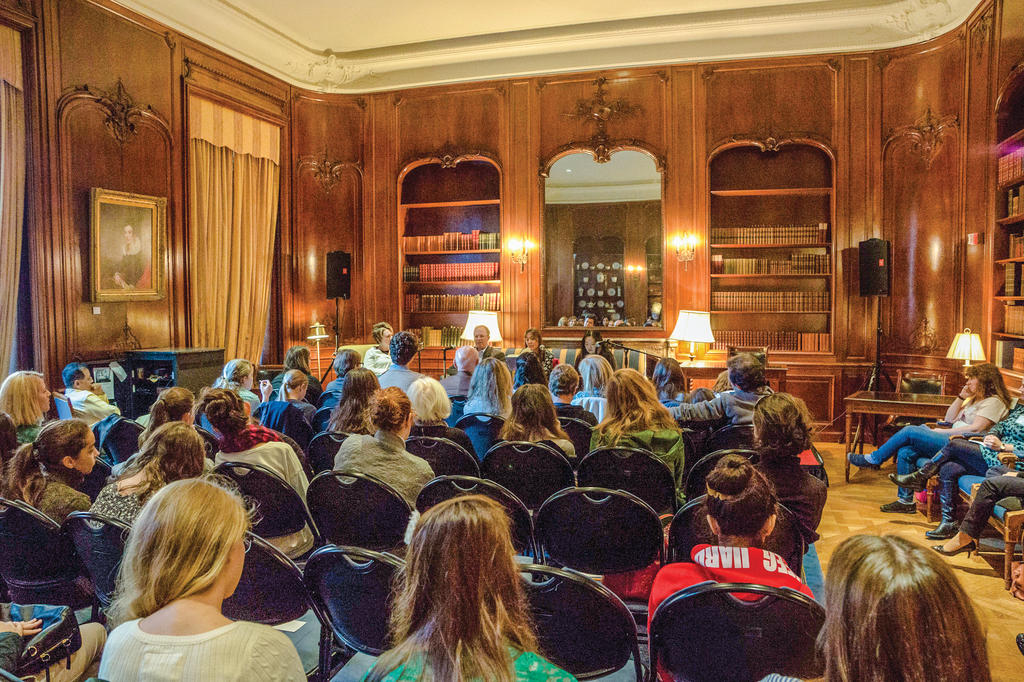 A group of people sit and listen to speakers in a wood paneled room at the New York Society Library