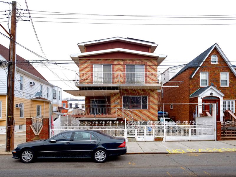 A multi-colored house with a decorative white fence in Queens