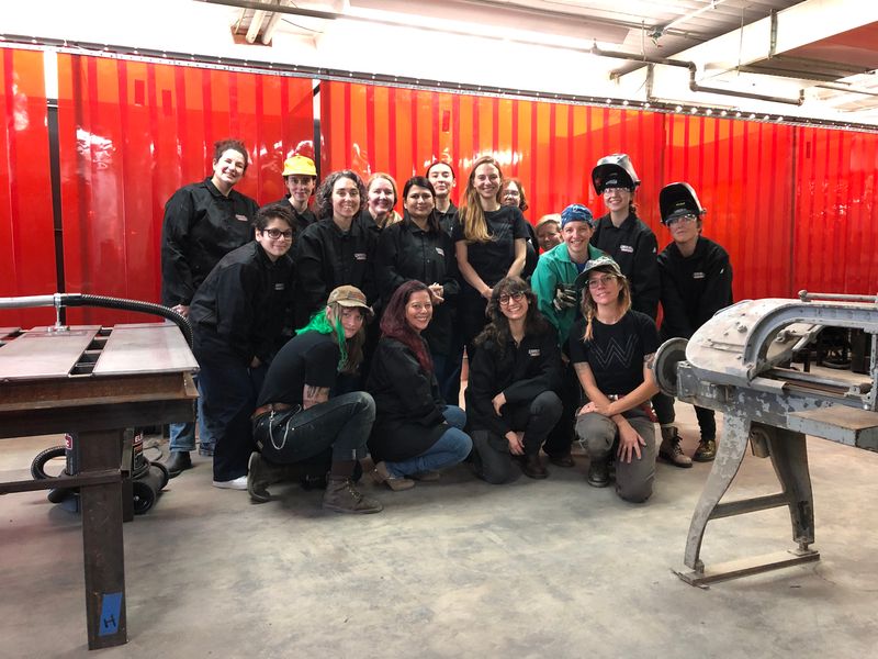 A group of women posed together for a photo inside the Women Who Weld Workshop