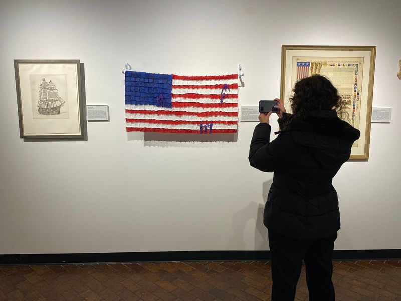 A woman takes a photo of art hanging on a wall