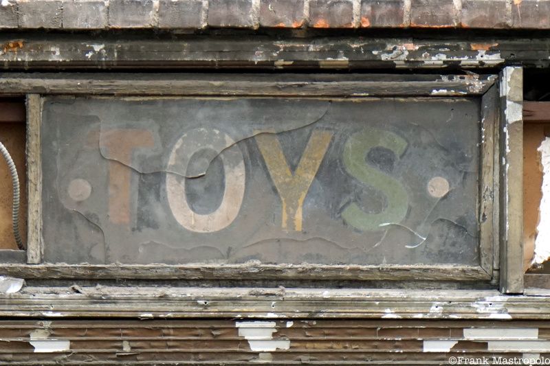 A ghost sign that says "Toys" in with each color a different letter