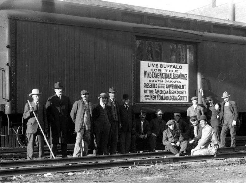 Black and white photo of a group of men standing outside a train car