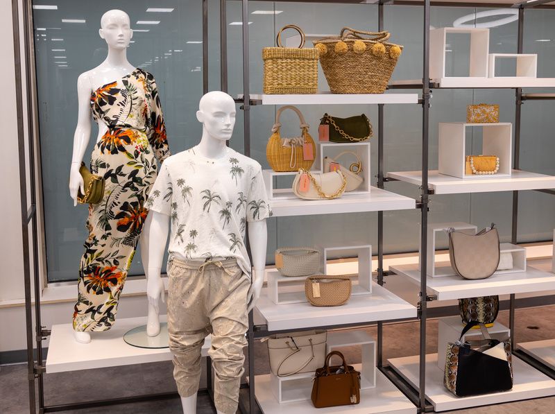 Two mannequins stands in front of shelves of purses