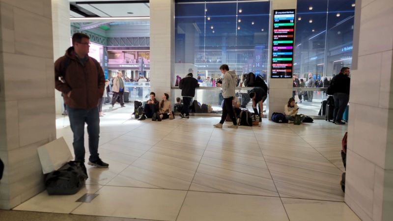 Riders sitting on the floor at Moynihan Train Hall while dealing with holiday travel in NYC