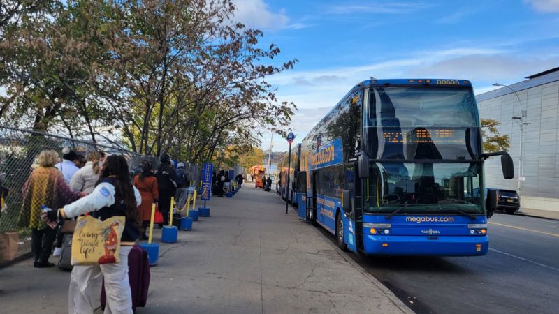 A line of people waiting to board a bus that waits at the curb during holiday travel in NYC