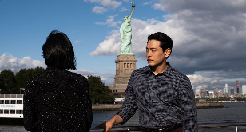 Greta Lee and Teo Yoo in front of the Statue of Liberty