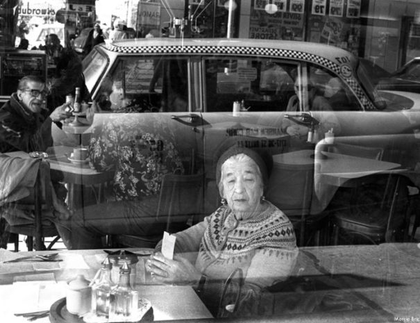 A women looks out the window of Dubrow's Cafeteria and taxi cab is reflected in the window