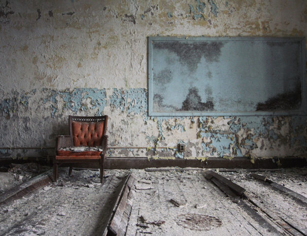 Abandoned room with peeling paint and a dusty red chair