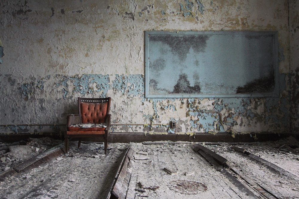 Abandoned room with peeling paint and a dusty red chair