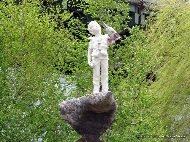 Pictured is a close-up of the boy, standing "high and dry", on the rocks facing the river.