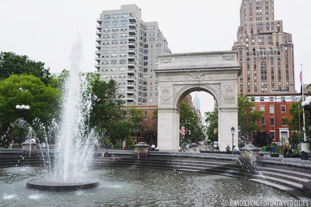 Water shoots up from the fountain in front of the Washington Square Arch