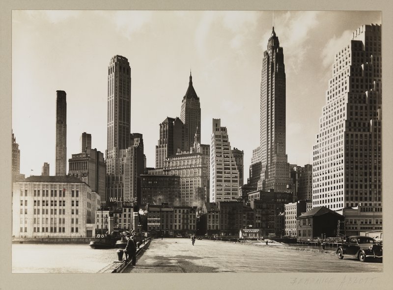 View of the contrast of 19th century dockside buildings and 20th century skyscrapers taken from Pier 11 on the East River, between Old Slip and Wall Street. The four tallest buildings are (from left to right): The Farmers Trust Building, the Bank of Manhattan, 60 Wall Tower, and 120 Wall Street.