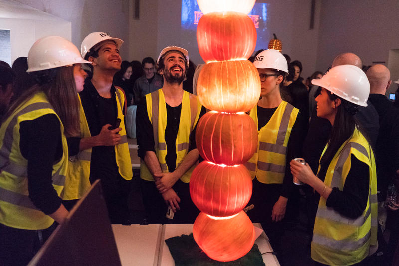 A team of architects in white hard hats and yellow vests surround a stack of glowing pumpkins for a favorite Halloween event in NYC.
