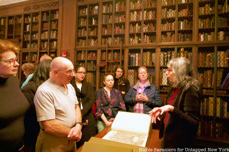 A group of Untapped New York Insiders gather around a historical anatomical text in the rare book room of the Academy of Medicine