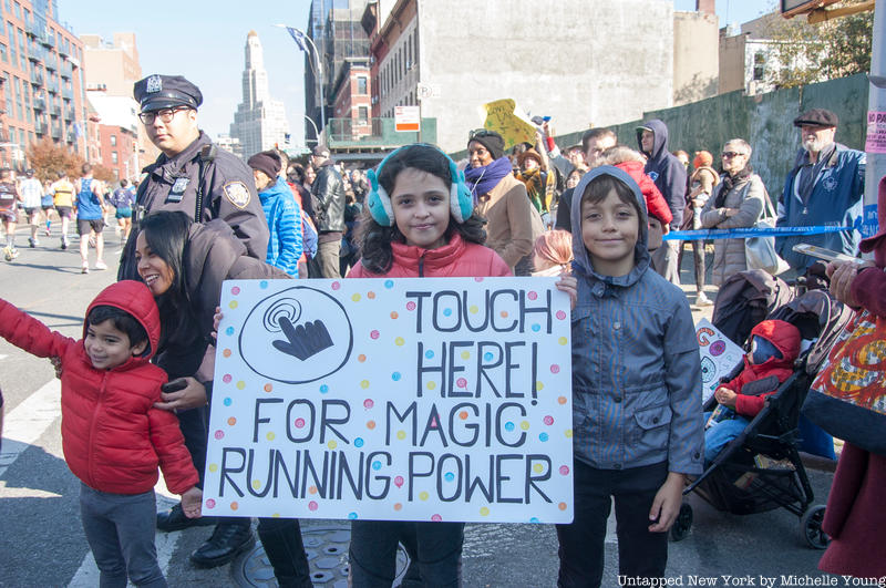 A group of kids hold up a sign on the side of the NYC Marathon course that reads "Touch Here for magic running power"