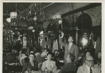 Dinners sit at tables inside Gage & Tollner as a staff member lights the gas fixtures overhead