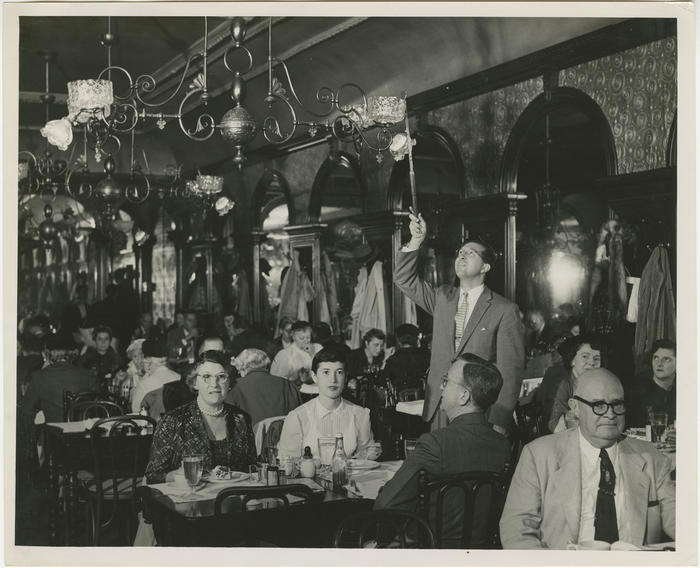 A staff members lights the gas lamps at Gage & Tollner amid diners in the restaurant