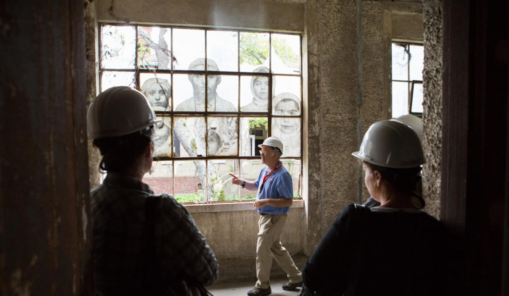 Guests in hard hats view an art installation inside Ellis Island's abandoned hospital
